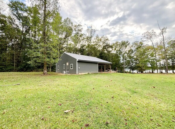 A single-story building with a covered porch, surrounded by a grassy field and trees.