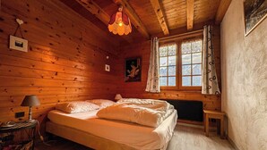 A cozy wooden cabin bedroom with a bed, a lamp, a picture frame, and a window with curtains. - Chalet facing Mont Blanc, calm and comfort (Saint-Gervais-les-Bains)