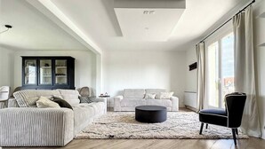 Un salon spacieux avec un plafond haut, un meuble sombre, un canapé à rayures, une table basse ronde et un fauteuil noir.