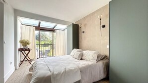 Une chambre avec un lit, une petite table sur laquelle est posée une plante, et une vue à travers une porte vitrée.