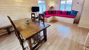 A wooden cabin interior with a dining table, chairs, a TV, and a red sofa. - Chalet le Petit Coeur (Xonrupt-Longemer)