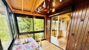 A wooden cabin with a dining area featuring a table with a checkered tablecloth and a wooden chair. - Chalet le Petit Coeur (Xonrupt-Longemer)