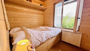 A wooden cabin room with a bed, a window, and a radiator. - Chalet le Petit Coeur (Xonrupt-Longemer)