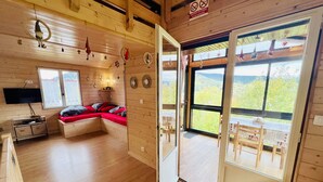 A cozy cabin interior with a wooden interior, a sofa bed with red cushions, a flat-screen TV, and a dining area with a table and chairs. - Chalet le Petit Coeur (Xonrupt-Longemer)