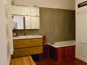 Bathroom features a vanity with a mirror and drawer, a bathtub with a wooden base, and a towel rack.