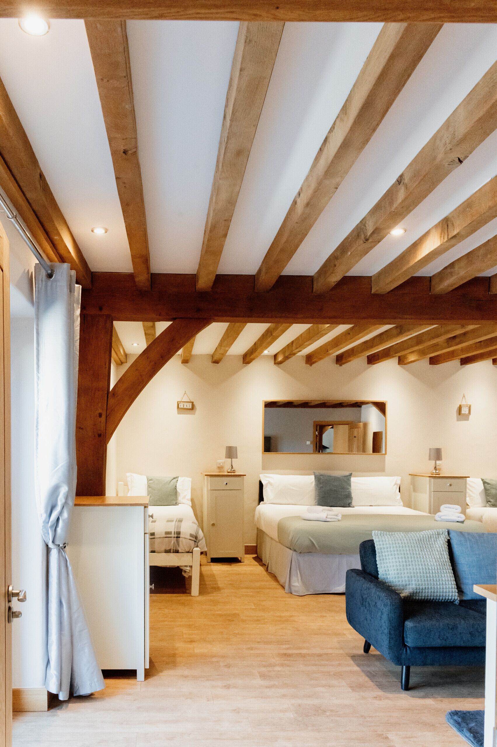 Ein Schlafzimmer mit Holzboden, einem Bett mit weißer Bettwäsche, einem blauen Sessel und einem Nachttisch mit Lampe.