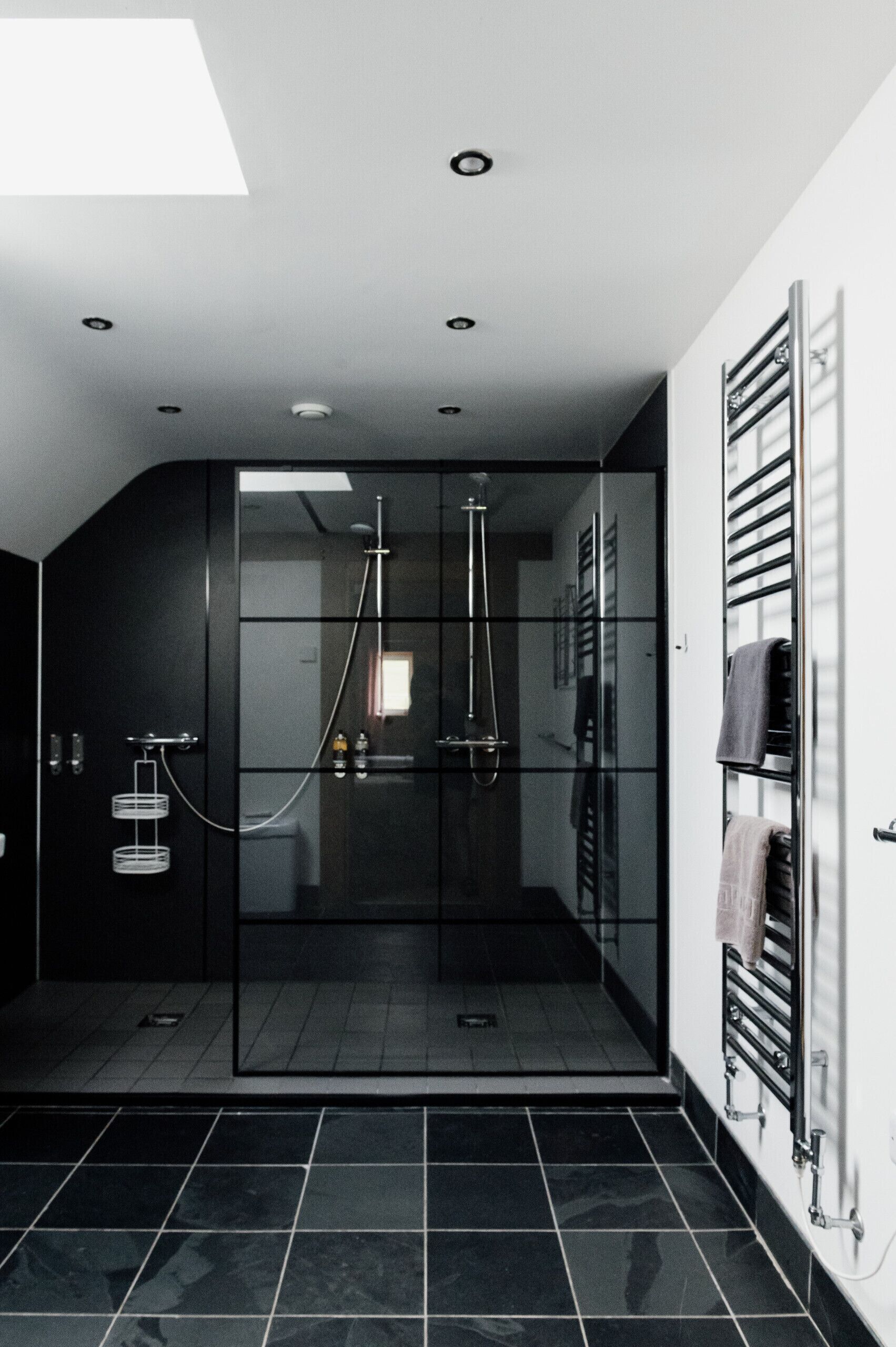 A modern bathroom with a glass-enclosed shower, black tiled flooring, and a towel rack on the wall.