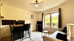 A cozy living room with a sofa, a dining area with a table and chairs, a TV, and a balcony with curtains. - Le Refuge des Skieurs (Combloux)