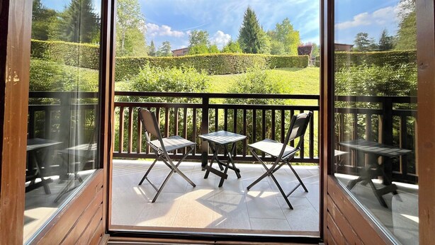 A balcony with two tables and two chairs, overlooking a well-maintained garden with hedges and trees. - Le Refuge des Skieurs (Combloux)