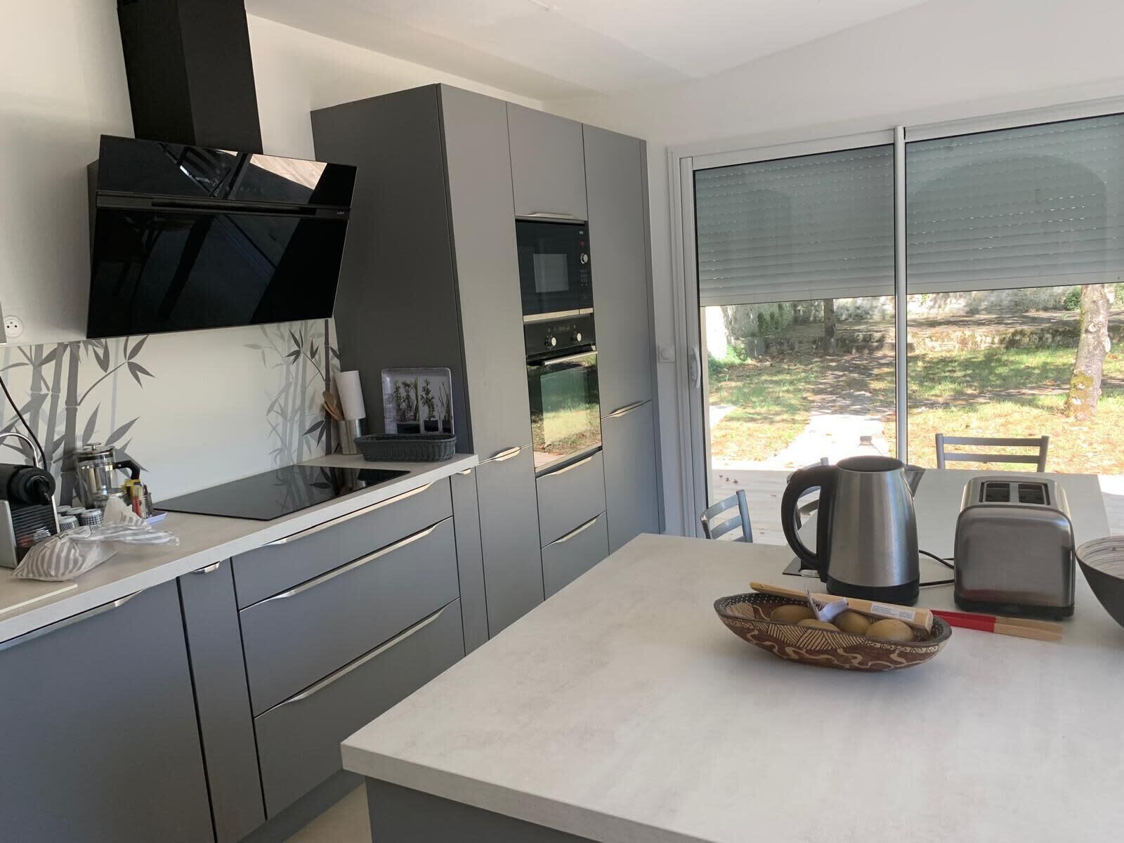 Een moderne keuken met grijze kastjes, een ingebouwde oven en een groot raam met uitzicht op de omgeving.