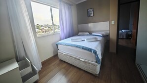 A bedroom with a bed, a window with curtains, a headboard, and a small painting on the wall.