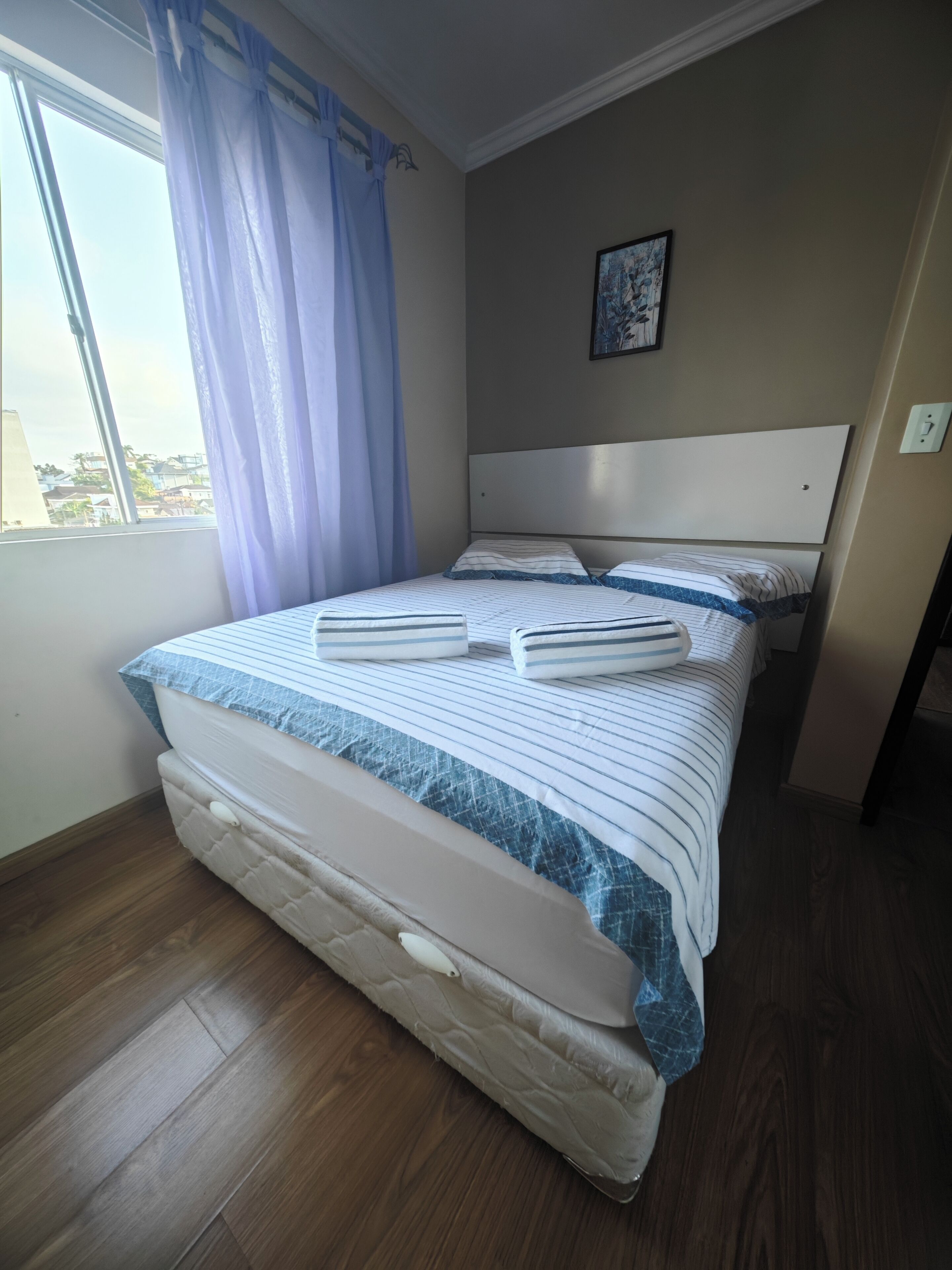 Een net opgemaakt bed met streepjesbeddengoed, een hoofdbord en een raam met gordijnen.