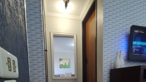 A hallway with wooden flooring, a wall-mounted thermostat, a framed artwork, a door, and a TV on a stand.