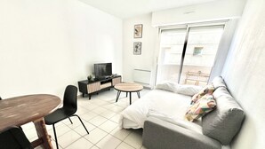 Un espacio habitable compacto con sofá, una pequeña mesa de comedor, televisor y ventana con vista al exterior.