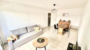 Una sala de estar con un sofá gris, una mesa redonda de madera y una mesa de comedor con sillas.