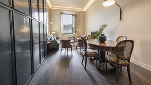 A dining area with a round table, wooden chairs, a potted plant, and a view through a window.