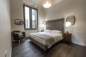 A bedroom with a bed, a chair, a nightstand, a lamp, and a window.