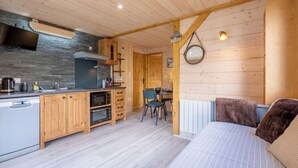 A compact kitchen with wooden cabinets, a built-in microwave, and a stove. There is a dining area with a table and chairs, and a bed with a striped blanket. - Mont Blanc chain view / hike / relaxation (Les Houches)