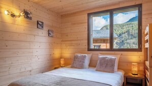 A wooden cabin bedroom with a bed, two bedside lamps, and a window with a mountain view. - Mont Blanc chain view / hike / relaxation (Les Houches)