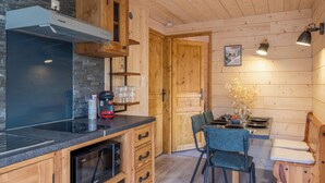 A compact kitchen with wooden cabinets, a Bosch coffee maker, a microwave, and a dining area with a table set for two. - Mont Blanc chain view / hike / relaxation (Les Houches)