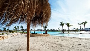 Una playa con piscina, palmeras y una sombrilla de paja.