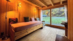 A cozy wooden cabin bedroom with a bed, a chair, a desk, and a large window offering a view of the outdoors. - Authentic family chalet with garden in Chamonix (Chamonix-Mont-Blanc)