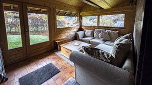 A cozy cabin interior with a wooden ceiling, a sofa, a coffee table, and large windows offering a view of the outdoors. - Authentic family chalet with garden in Chamonix (Chamonix-Mont-Blanc)