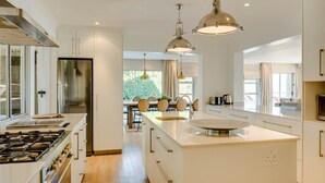 Een moderne keuken met een centraal kookeiland, roestvrijstalen apparatuur en hanglampen.