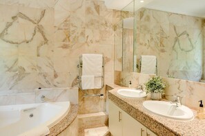 Un baño con pared de mármol, una bañera, un lavamanos, un espejo y una planta en maceta.