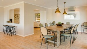 Een ruime eethoek met een houten tafel en stoelen, een bar met krukken, en hanglampen.