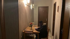 A narrow hallway with a wooden table and chairs, a vase with flowers, and a person sitting at the table. - ARTISHA TRAVEL HOTEL (Tbilisi)