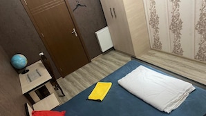 A bedroom with a blue bedspread, a white pillow, a red pillow, a yellow folder, and a globe on a small table. - ARTISHA TRAVEL HOTEL (Tbilisi)