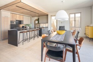 Une cuisine moderne dotée d’un îlot central, de meubles en bois et d’un coin repas avec une longue table et des chaises.