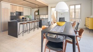 Een moderne keuken met een centraal eiland, houten kastjes, en een eethoek met een lange tafel en stoelen.