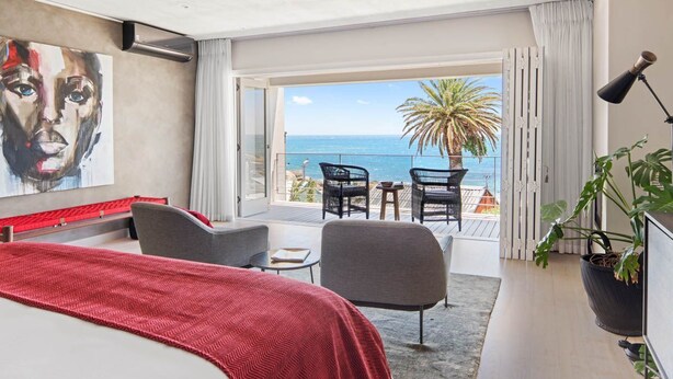 Een moderne hotelkamer met een groot bed, een balkon met uitzicht op zee en een schilderij aan de muur.