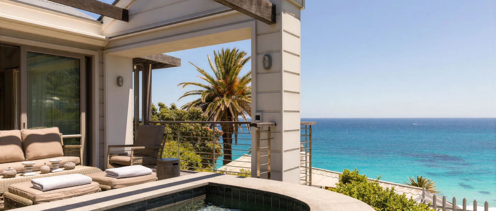 A balcony with a view of the ocean, a seating area with cushions, and a small pool.