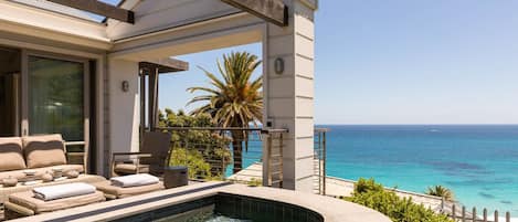 A modern outdoor pool area with lounge chairs, a clear view of the ocean, and a white building structure.