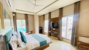 Ein Hotelzimmer mit einem großen Bett, einem an der Wand befestigten Fernseher, einem Deckenventilator und Blick ins Freie.