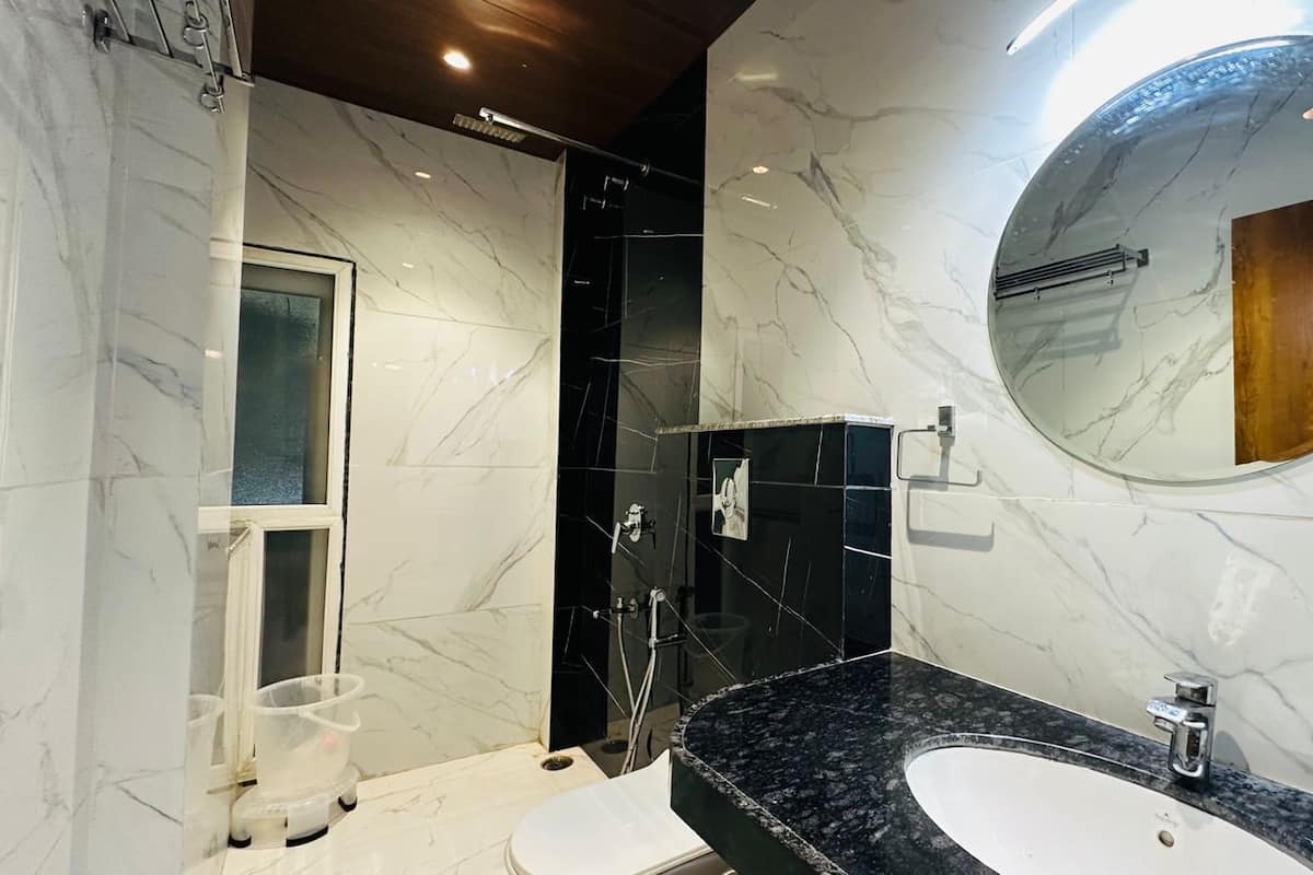 A modern bathroom with a marble vanity, a round mirror, and a glass-enclosed shower.
