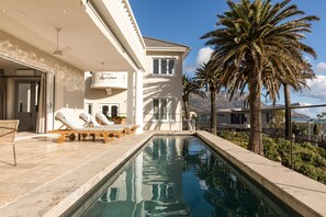 Un espace aménagé au bord de la piscine, avec des chaises longues, une piscine et des palmiers.