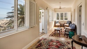 A sunlit hallway with large windows, a ceiling fan, and a patterned rug.