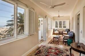 Un couloir baigné de lumière, avec de grandes fenêtres, un ventilateur de plafond et un tapis à motifs.