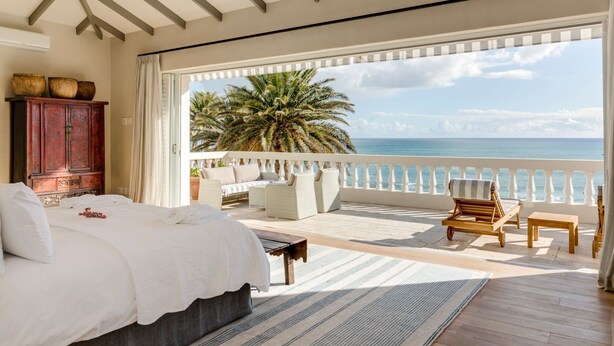 A bedroom with a large bed, a wooden coffee table, and a view of the ocean through a balcony.