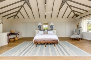 A spacious bedroom with a large bed, a wooden bench, a chair, and a console table with baskets.