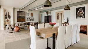 A spacious dining area with a wooden table and white chairs, a fireplace, and various artworks on the walls.