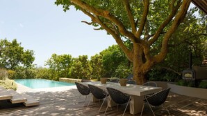 Ein Essbereich im Freien mit Pool, Holzterrasse und einem großen Baum.
