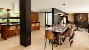 Eine moderne Küche mit einer zentralen Kochinsel, Barhocker und einem Essbereich mit einem Marmortisch und Stühlen.