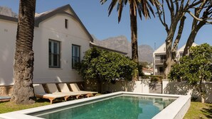 Une piscine entourée de chaises longues, de palmiers et d’un bâtiment blanc, avec une vue sur les montagnes en arrière-plan.