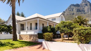 Une maison blanche de style colonial, dotée d’un porche à l’avant, de palmiers et d’une montagne en arrière-plan.