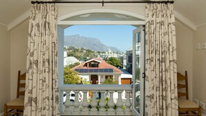 Une chambre avec un balcon, donnant sur des maisons, et avec une montagne en arrière-plan.